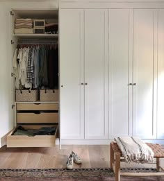 a white closet with drawers and clothes hanging on the wall next to a bench in front of it