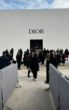 a crowd of people standing in front of a dior showroom building with the doors open