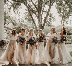 a group of women standing next to each other in front of a tree and holding bouquets