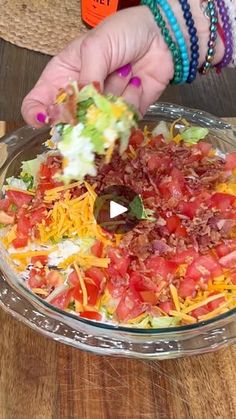 a person is adding toppings to a salad in a glass bowl