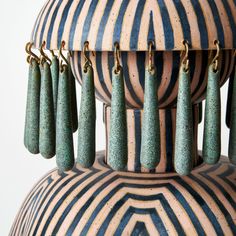 several green earrings hanging from the top of a large, striped vase with gold chains attached to them