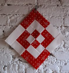 a red and white patchwork quilt hanging on a brick wall next to a pair of scissors