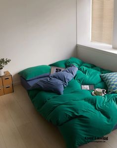 an unmade bed with green sheets and pillows in a white room next to a window