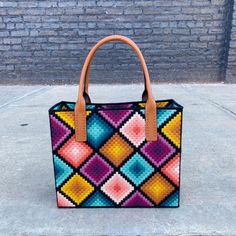 a multicolored handbag sitting on top of a cement floor next to a brick wall