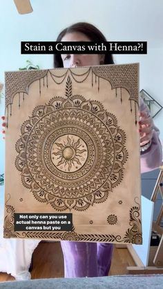 a woman holding up a piece of art that says stain a canvas with henna?