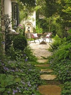 an image of a garden scene with flowers and plants in the foreground, along with a stone path leading to a patio