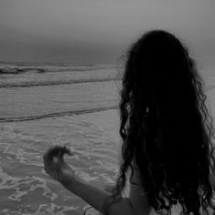 a woman standing in the ocean with her back to the camera looking at the waves