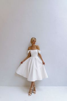 a woman in a white dress standing against a wall with her hands on her hips