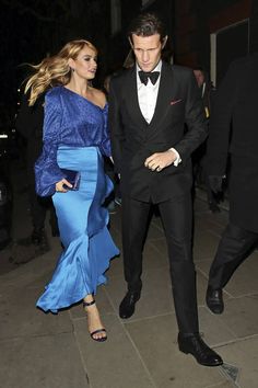 a man in a tuxedo walking next to a woman in a blue dress