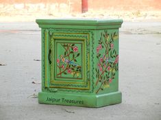 a small green box with flowers painted on it sitting in the middle of a street