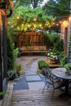 Cozy backyard with a wooden bench, string lights, and lush greenery. Features a stone pathway, potted plants, and a round table with chairs. Patio Home Backyard Ideas, Small Fenced In Backyard Ideas, Small Backyard Ideas Diy, Mini Backyard Ideas, Small Porch Garden, Small Back Patio Ideas, Small Backyard Patio Designs, Townhouse Courtyard