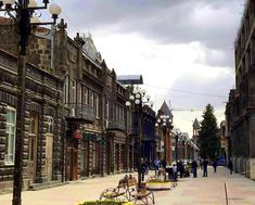 an empty city street with people walking and sitting on benches in front of old buildings