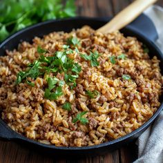 a skillet filled with rice and meat on top of a wooden table next to parsley