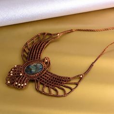 a necklace with a bird on it and a blue stone in the center is sitting on a gold cloth