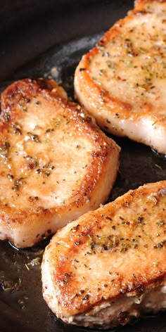 three pork chops cooking in a skillet with seasoning sprinkled on them