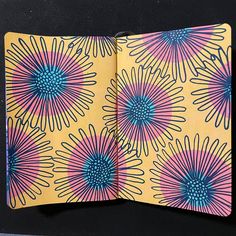 an open notebook with colorful flowers on yellow and blue paper in front of a black background