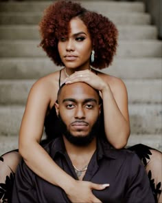 a man and woman sitting next to each other in front of some stairs with their arms around one another