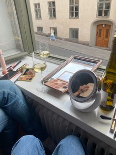 a person sitting at a window sill with their feet on the windowsill and wine glasses in front of them