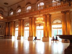 two people sitting on benches in the middle of a large room with chandeliers