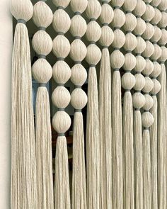 a wall with many balls and tassels hanging from it's sides in front of a window