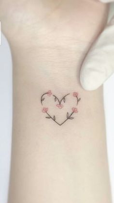 a small heart tattoo with flowers on the side of the wrist and an arrow in the middle