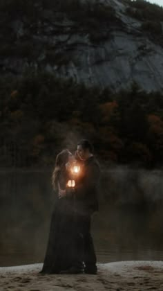 a man and woman standing next to each other in front of a mountain at night