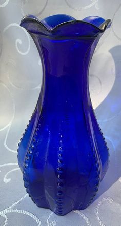 a blue glass vase sitting on top of a white tablecloth with swirly designs