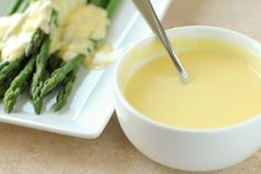 asparagus and cheese on a plate next to a bowl of soup with a spoon