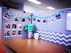 an office cubicle decorated with pictures and flowers on the wall, along with photos hanging from clothes pins