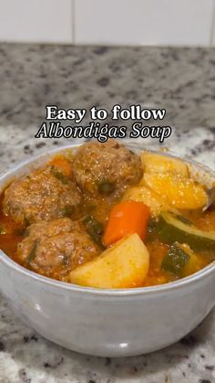 a bowl filled with meatballs and vegetables on top of a marble counter next to a white tile wall