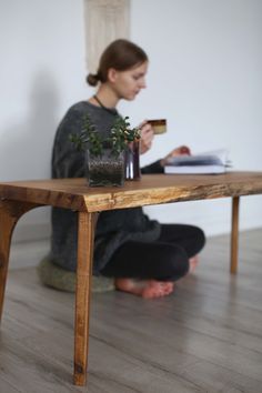 a woman sitting on the floor next to a wooden table with a plant in it