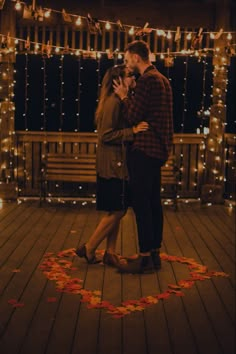 a man and woman kissing in front of string lights on a wooden deck with petals around them