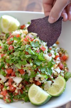 a person is dipping a tortilla into a bowl filled with vegetables and cilantro