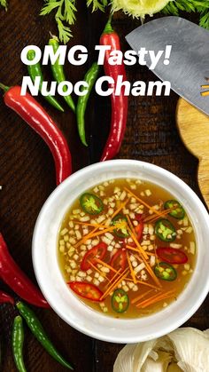 a white bowl filled with soup next to red peppers and green peppers on top of a wooden table