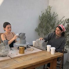 two women sitting at a table working on pottery