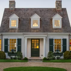 a white house with green shutters and two large windows on the front, surrounded by grass