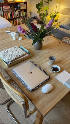 a laptop computer sitting on top of a wooden table next to a vase filled with flowers