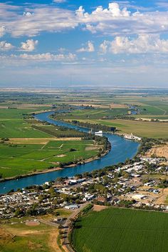 an aerial view of a river running through a green field next to a rural town