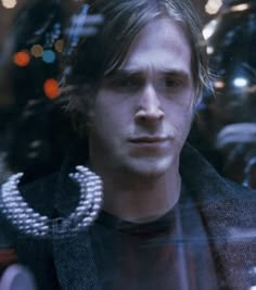 a man looking through a glass window with beads on his collar and necklace around his neck