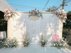 an outdoor wedding setup with flowers and greenery on the wall, surrounded by white drapes