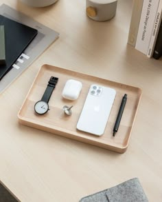 a wooden tray with an apple watch, cell phone and other items on it sitting on a table