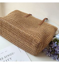 a straw bag sitting on top of a table next to a book and purple flowers