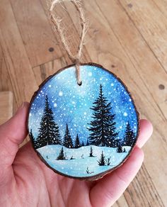 a hand holding a painted ornament with trees in the snow and stars on it