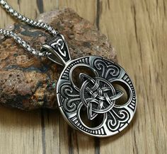 a silver pendant with an intricate design on it sitting on top of a wooden surface