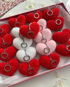 many red and white crocheted hearts are in a pink box with silver rings