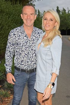 a man and woman standing next to each other in front of some bushes with trees