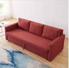 a red couch sitting on top of a hard wood floor next to a white wall