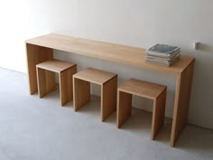 a wooden table with three stools and a book on the top one is next to a white wall