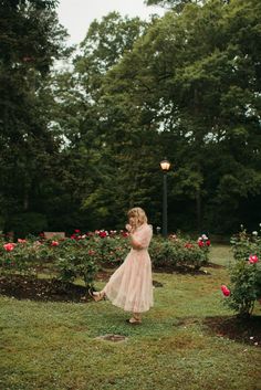 a woman in a pink dress is walking through a garden with roses on the ground