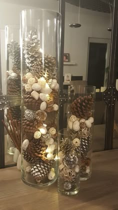 two tall glass vases filled with pine cones and other decorations on top of a wooden table